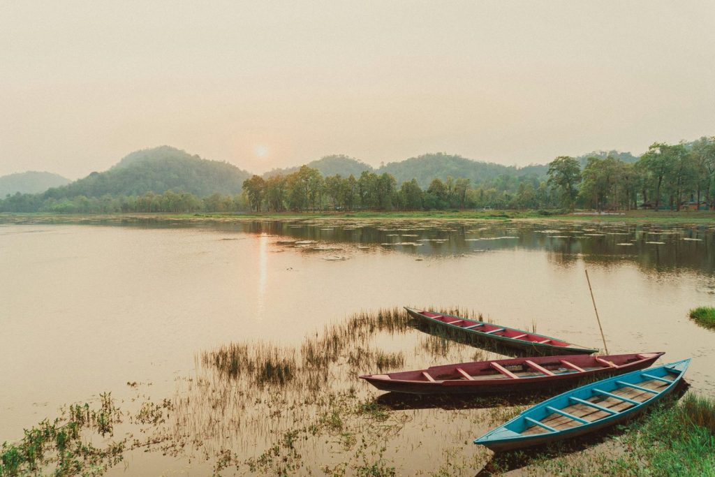 Peaceful lake scene with boats and green hills at sunset in Assam, India.