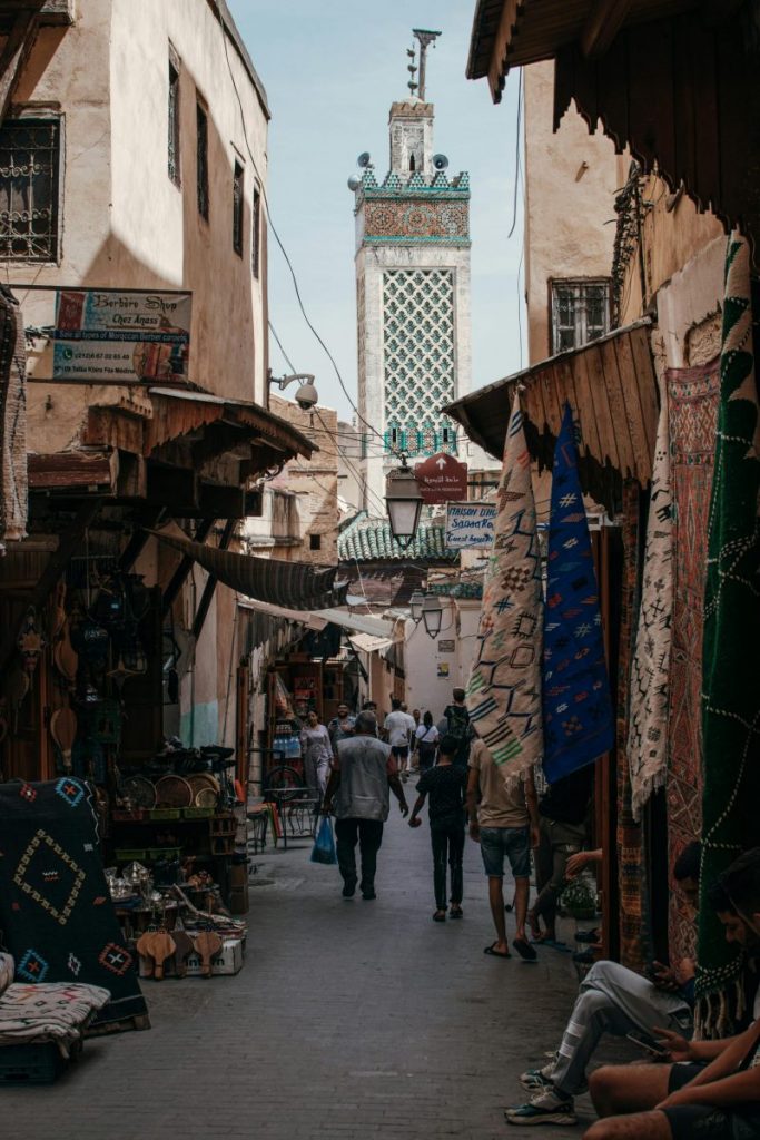 Explore the bustling narrow alley of a Moroccan bazaar with shops and vibrant textiles.