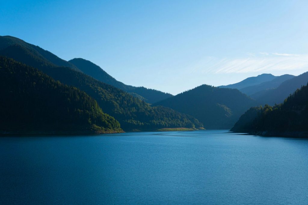 Tranquil lake surrounded by lush green mountains in Retezat National Park, Romania.